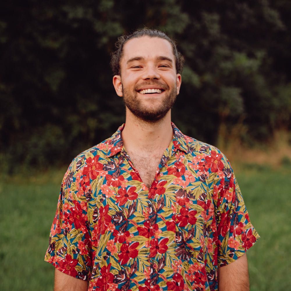 A man with a beard is wearing a colorful floral shirt and smiling.