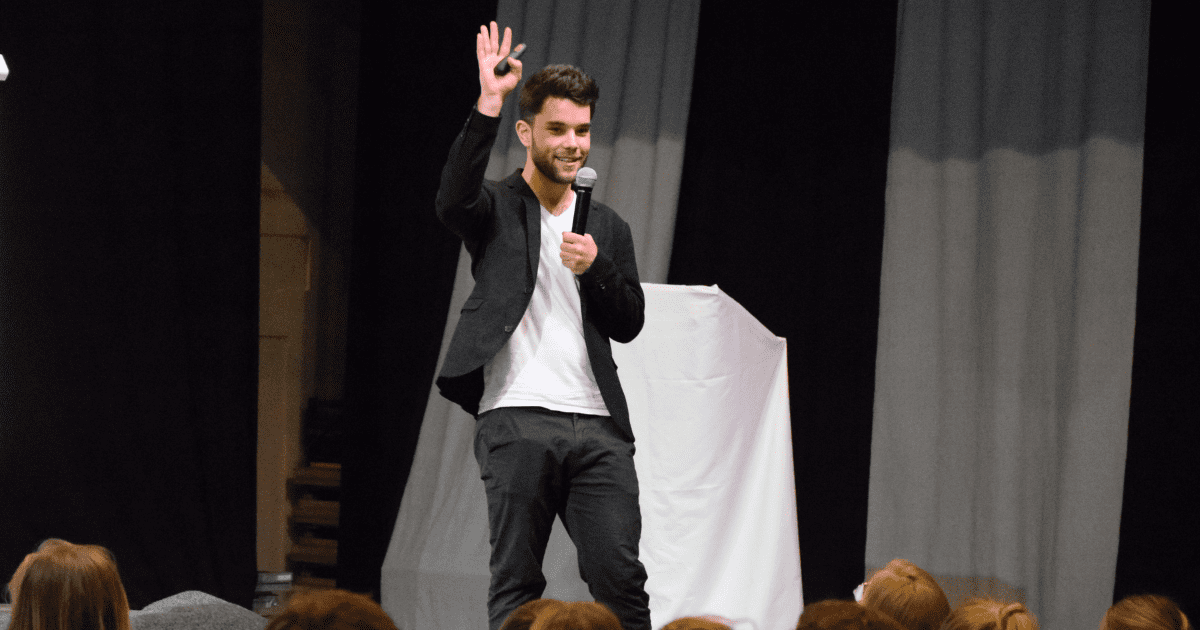 A man is standing on a stage holding a microphone in front of a crowd.