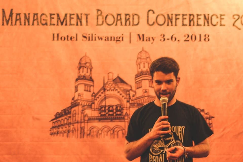 A man is holding a microphone in front of a sign that says management board conference