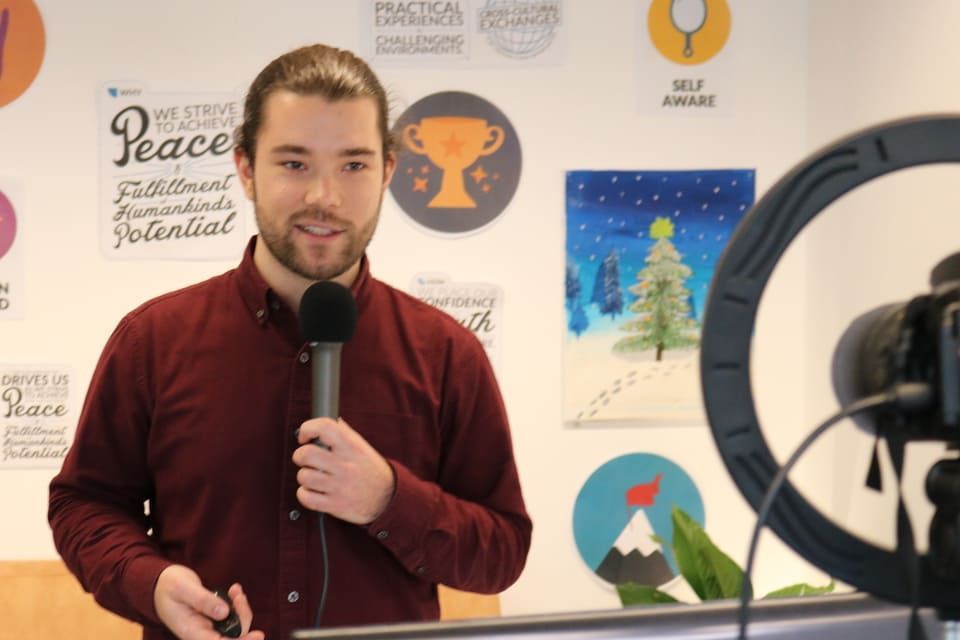 A man in a red shirt is holding a microphone in front of a camera.