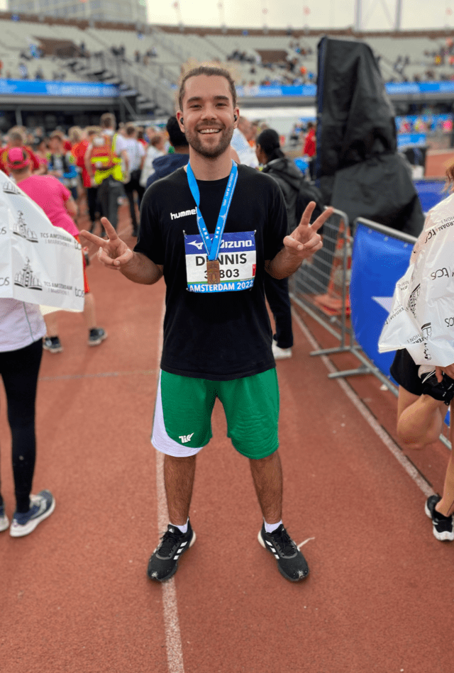 A man in a black shirt and green shorts is standing on a track with a medal around his neck.