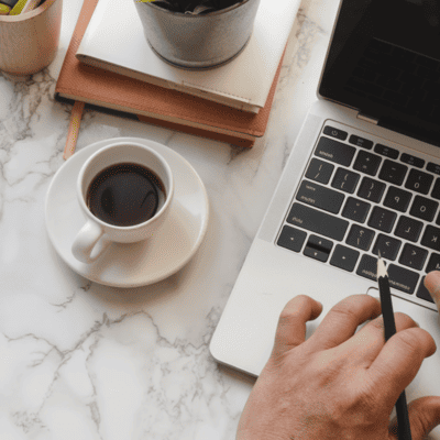 A person is using a laptop computer on a marble table next to a cup of coffee.