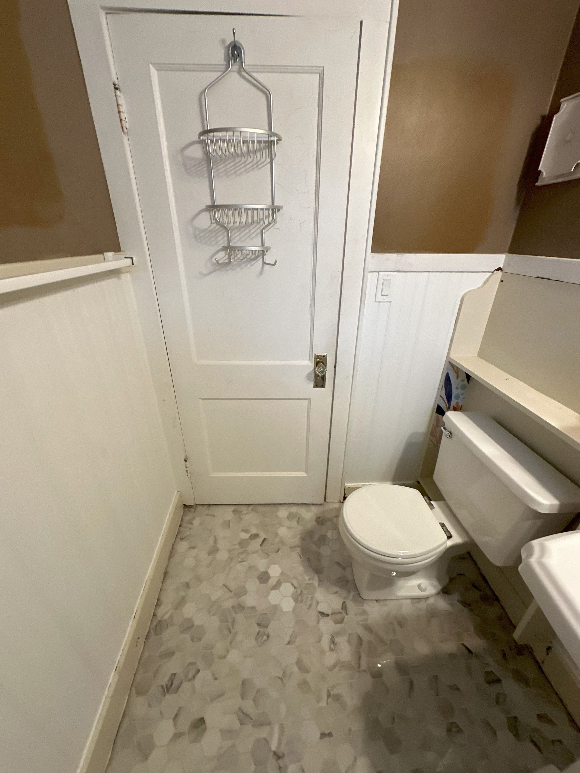a bathroom with a toilet and a shower caddy hanging on the door .