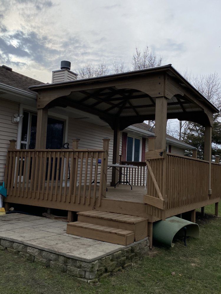 a wooden deck with a gazebo on top of it in front of a house .