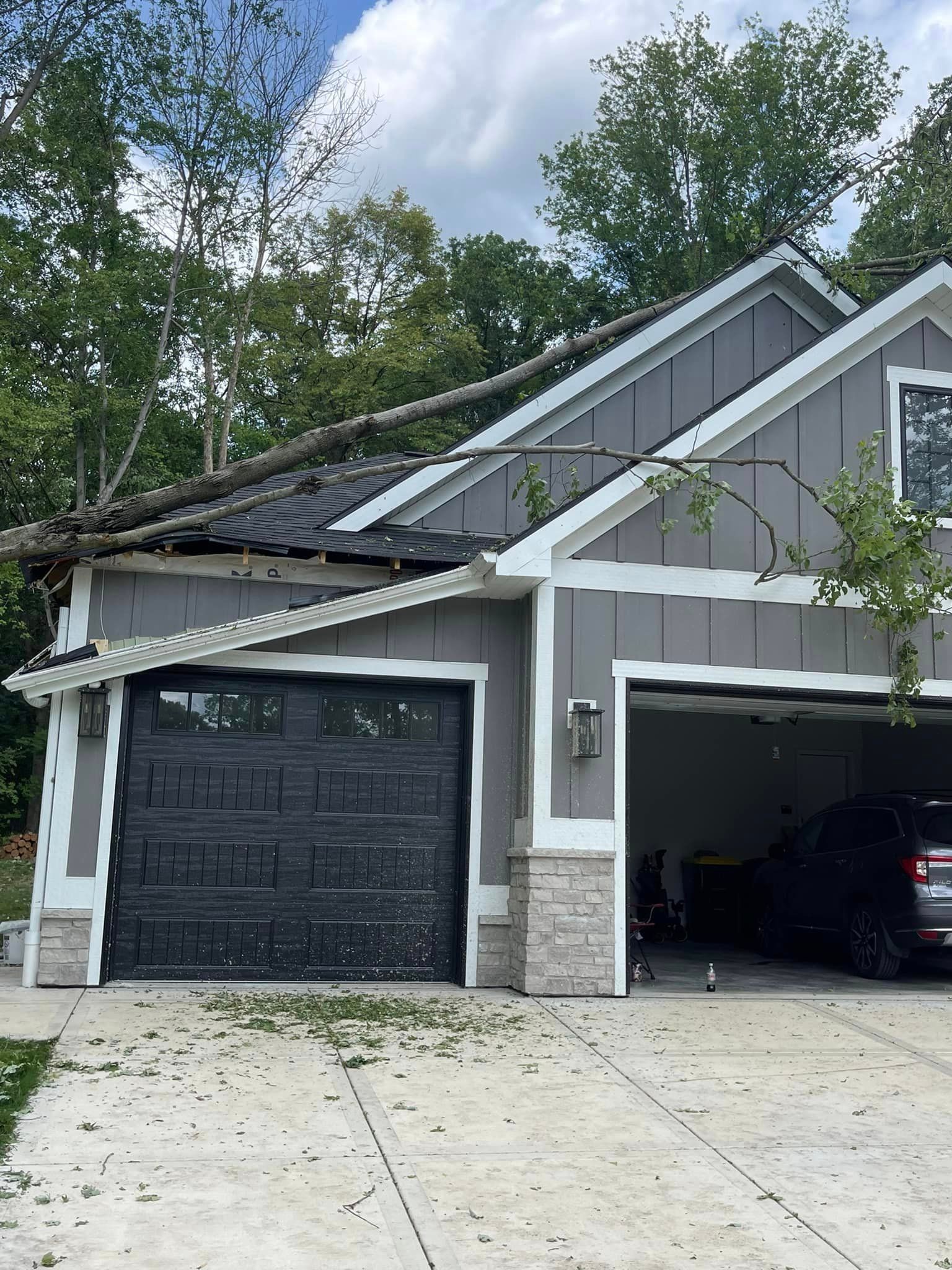 A house with a tree fallen on it and a car parked in front of it.