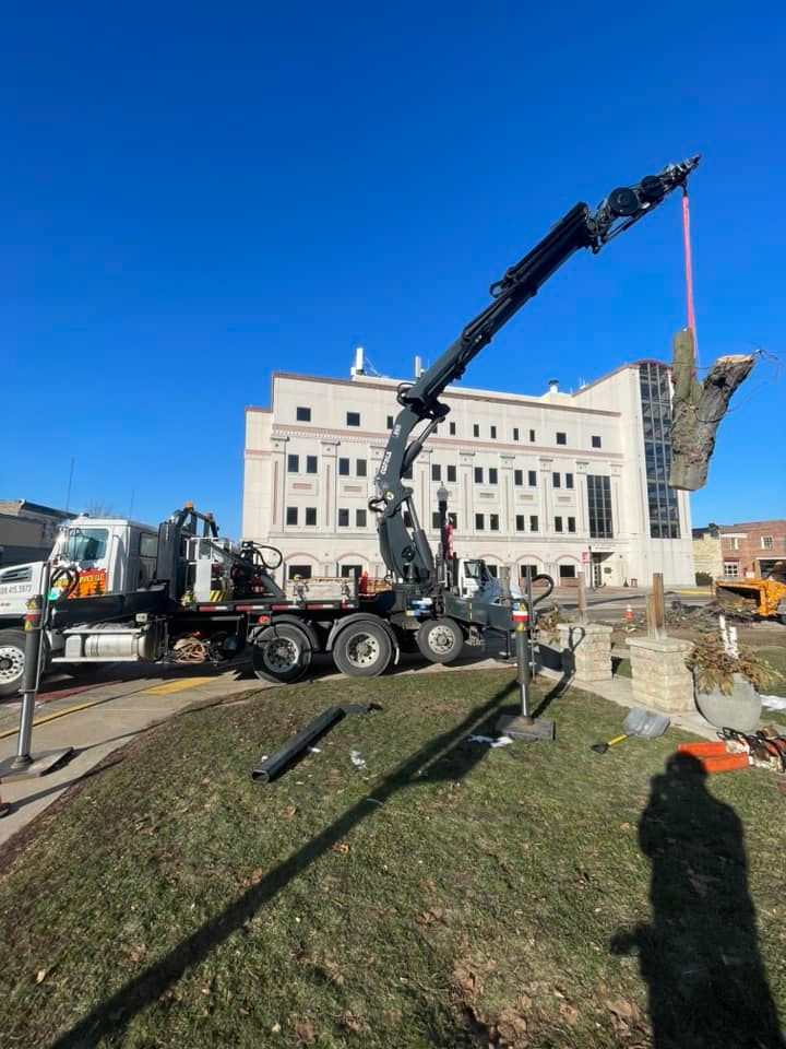 A truck with a crane attached to it is lifting a statue in front of a building.