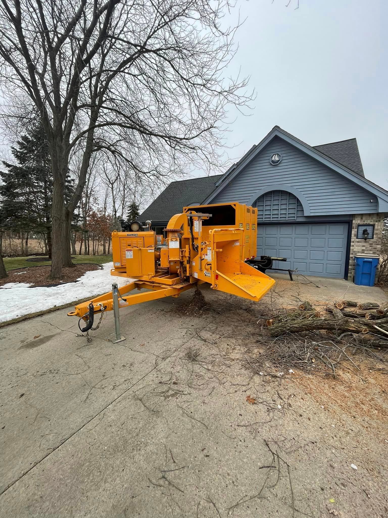 A yellow tree chipper is parked in front of a house.