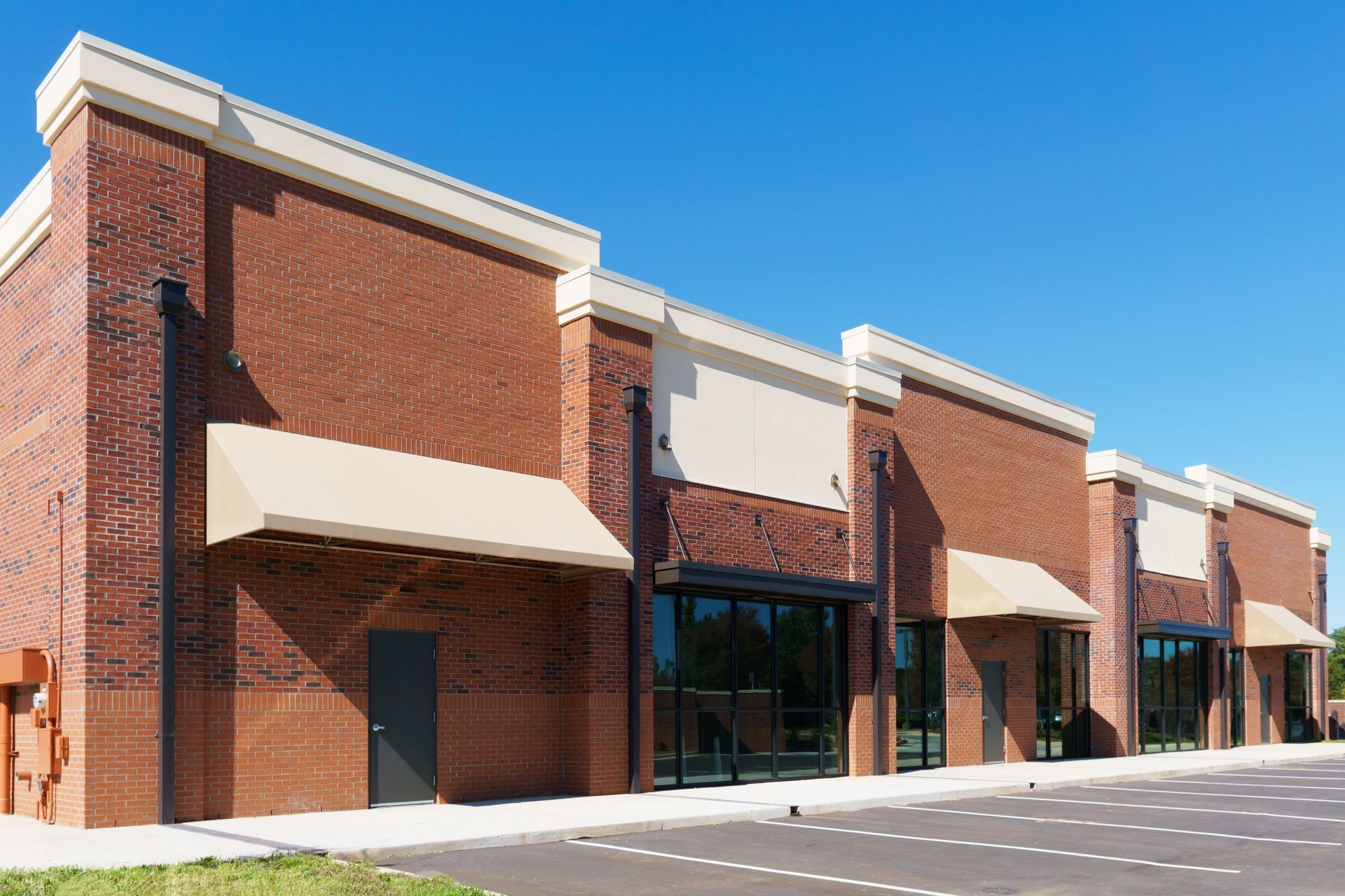 A row of brick buildings with awnings and a parking lot in front of them.