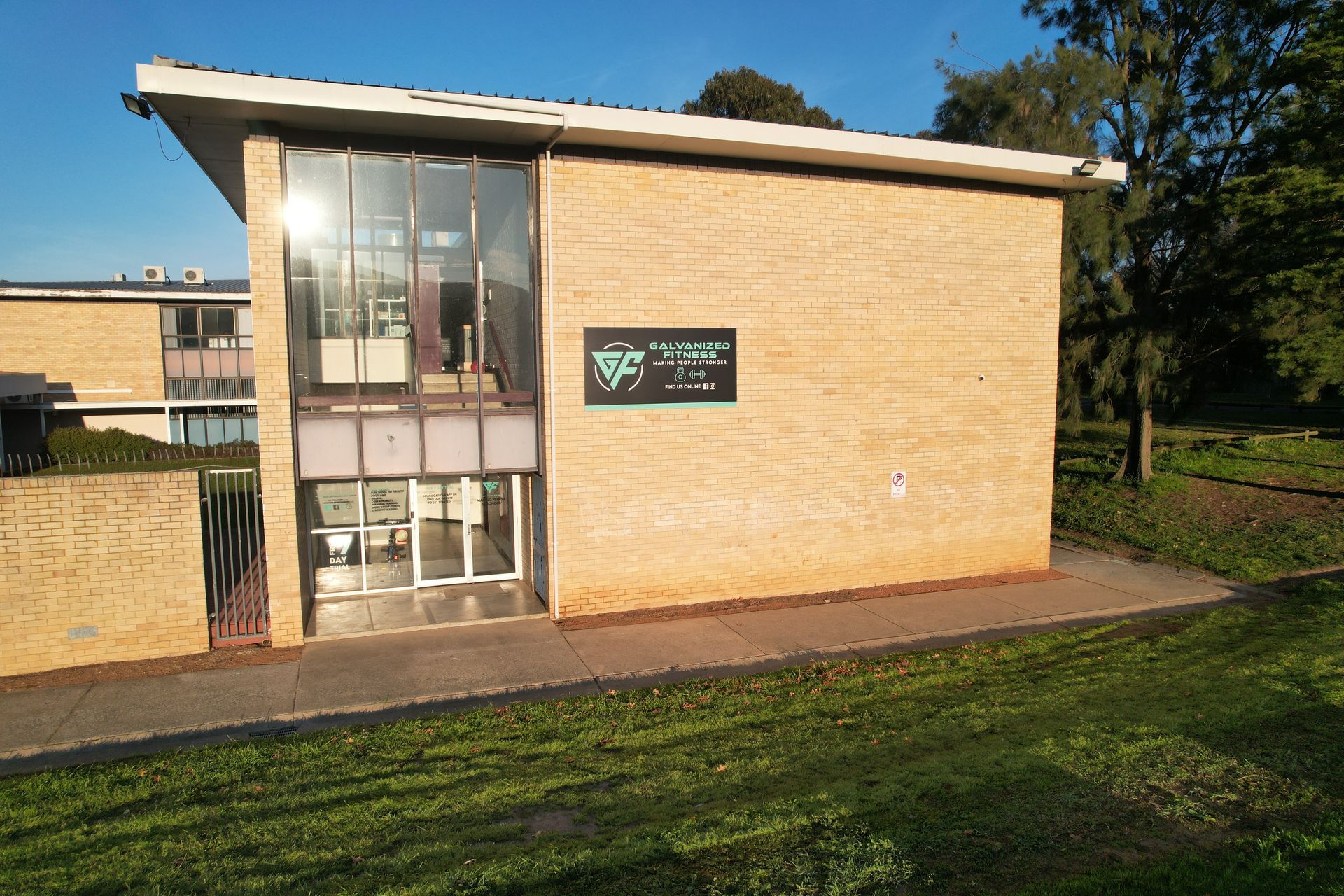 Building with glass windows and a sign, set in a grassy area, under a blue sky.