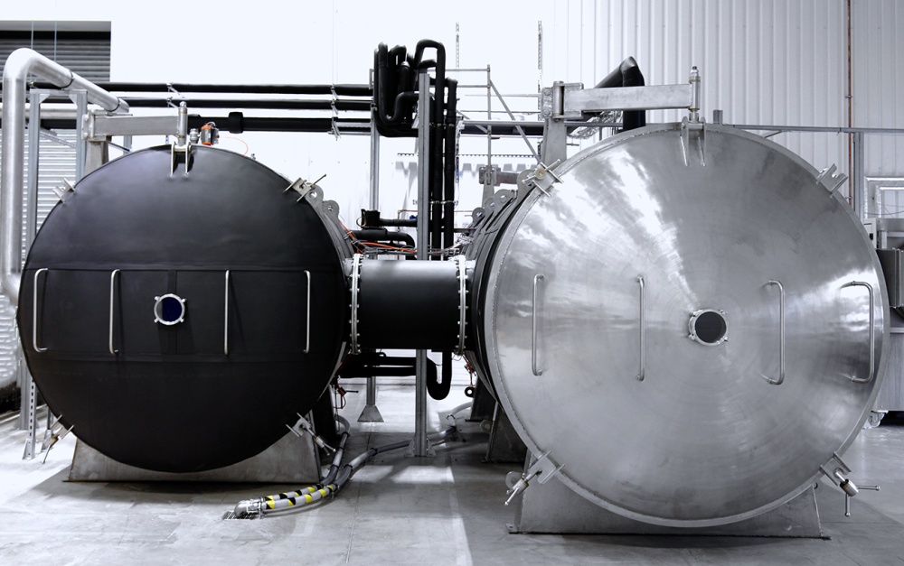 Two large industrial tanks connected by pipes in a factory setting. One is black, the other silver.