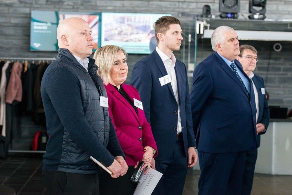 Group of five people, wearing business attire, standing indoors and looking forward.