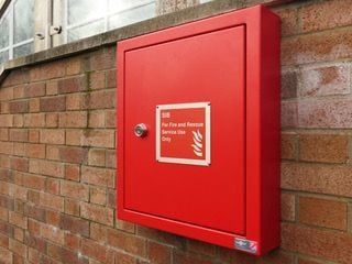 Red fire hose cabinet mounted on a brick wall, labeled