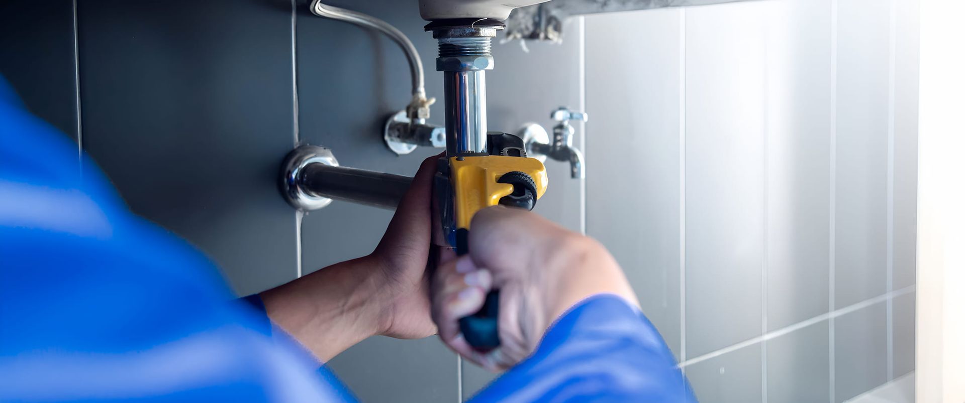 A Plumber Is Fixing A Sink In A Bathroom With A Wrench — GPS Plumbing, Drainage & Gasfitting In Dubbo, NSW