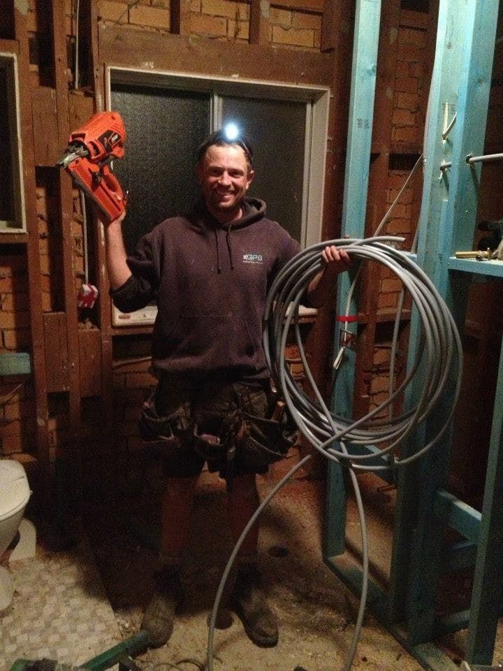 A Smiling Person Wearing a Hoodie and Headlamp Stands in a Dimly Lit Construction Area