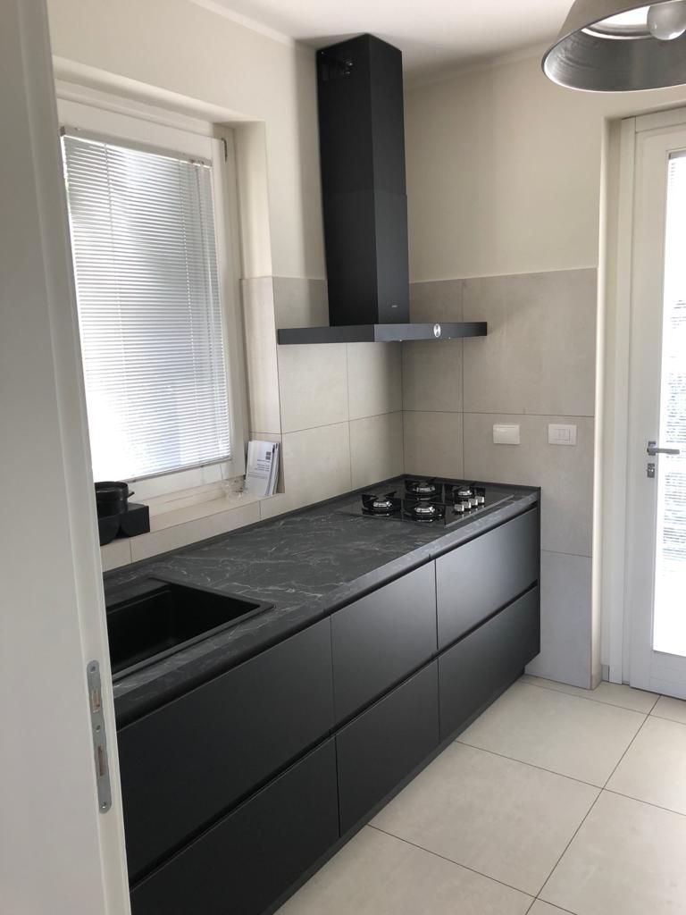 Moderna cucina nera con mobili, piano cottura, cappa e finestra.