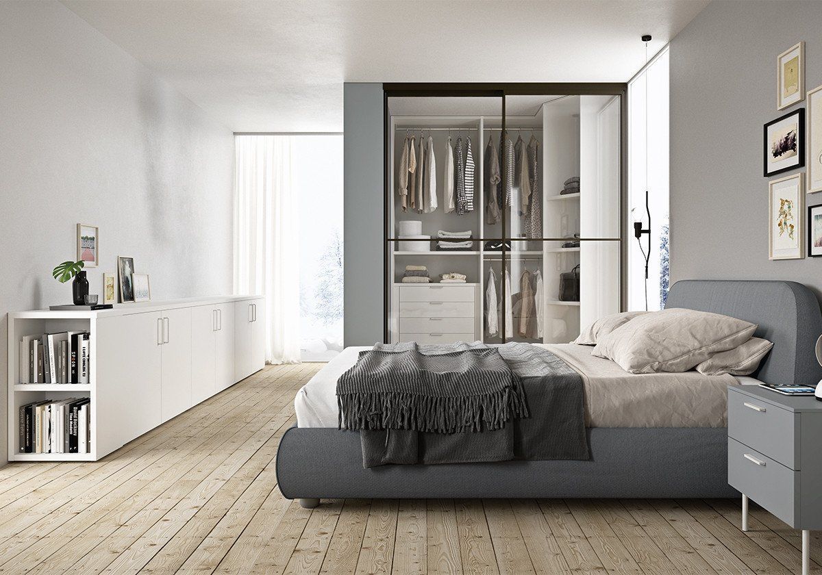 Camera da letto moderna con letto grigio, armadio a muro, pavimenti in legno e credenze bianche.