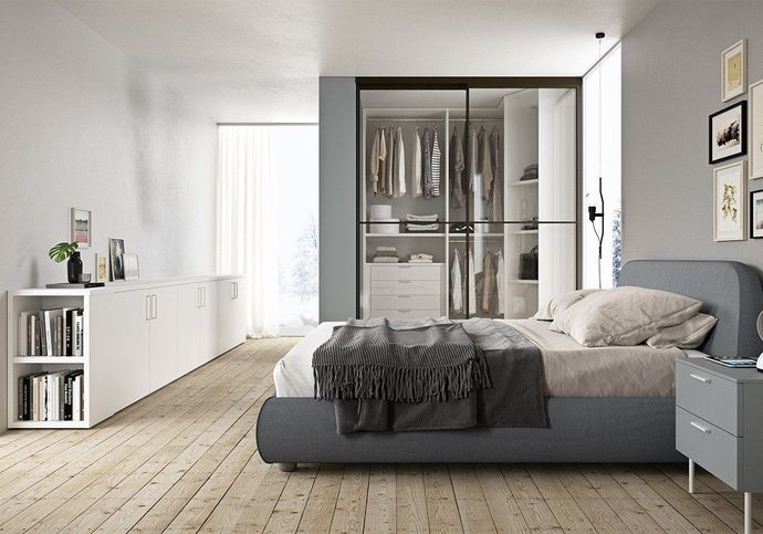 Camera da letto moderna con letto grigio, armadio a muro, pavimenti in legno e credenze bianche.