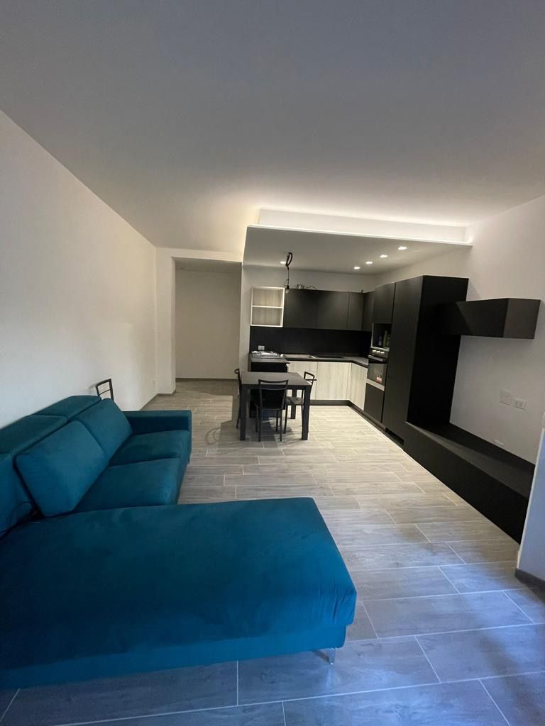 Un appartamento moderno con divano verde acqua, cucina bianca e nera e zona pranzo.