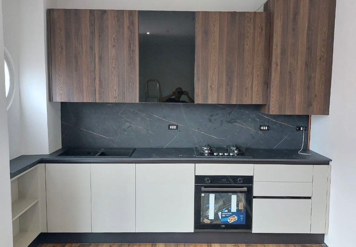 Cucina moderna con pensili in legno scuro, pensili color crema, piano di lavoro scuro e paraschizzi nero.