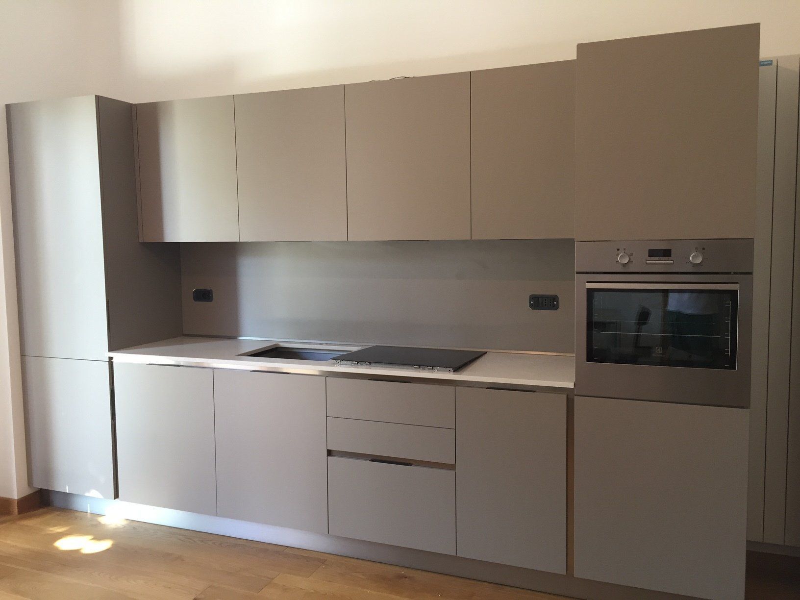 Cucina moderna con mobili grigi, forno incorporato e piano di lavoro bianco.