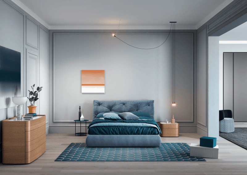 Camera da letto con pareti grigie, letto blu, opere d'arte, mobili in legno e tappeto blu a fantasia.