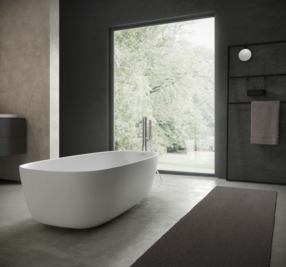 Bagno moderno con vasca bianca, ampia finestra con vista sul verde, pareti scure e tappeto grigio.