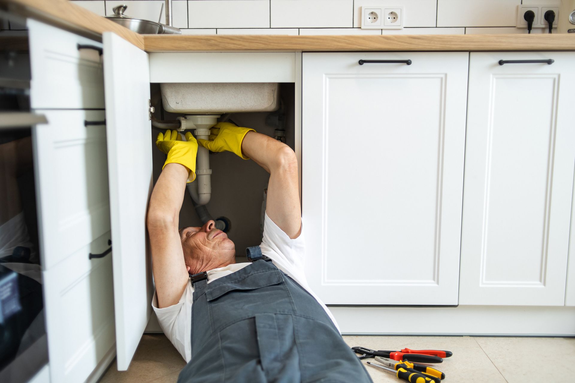 A man wearing yellow gloves and overalls is repairing a sink, highlighting the plumbing technician. A man wearing yellow gloves and overalls is repairing a sink, highlighting the plumbing technician.