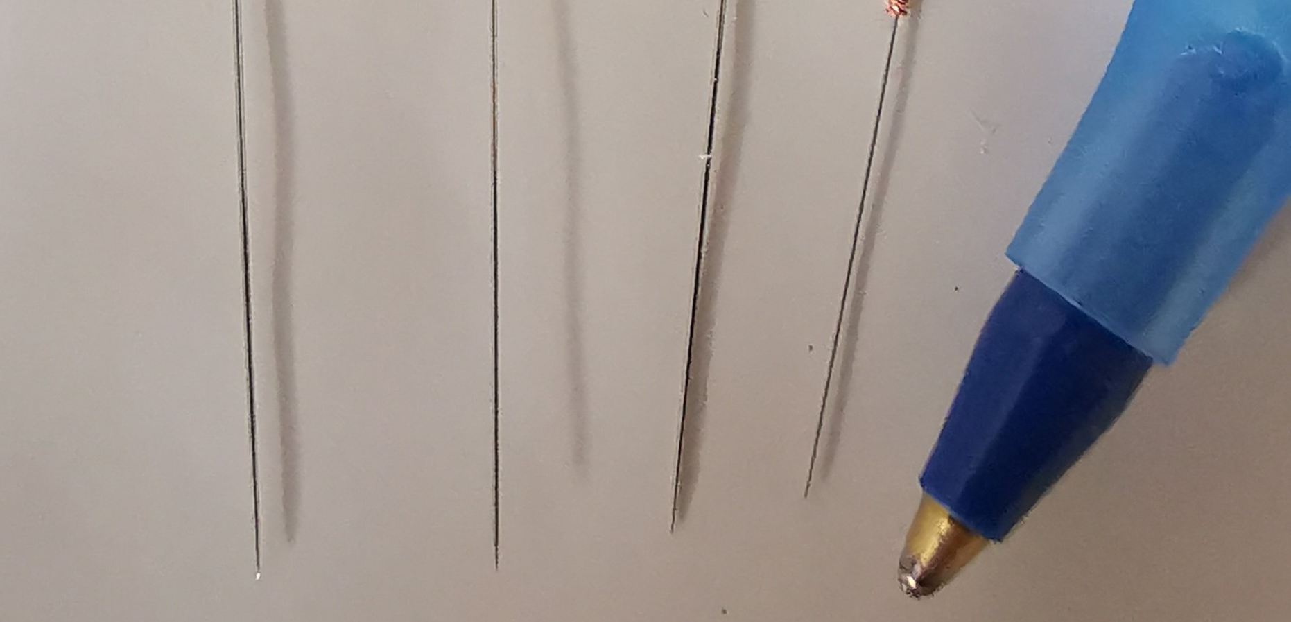Vier dunne, draadachtige metalen sondes liggen op een wit oppervlak naast de punt van een blauwe balpen.