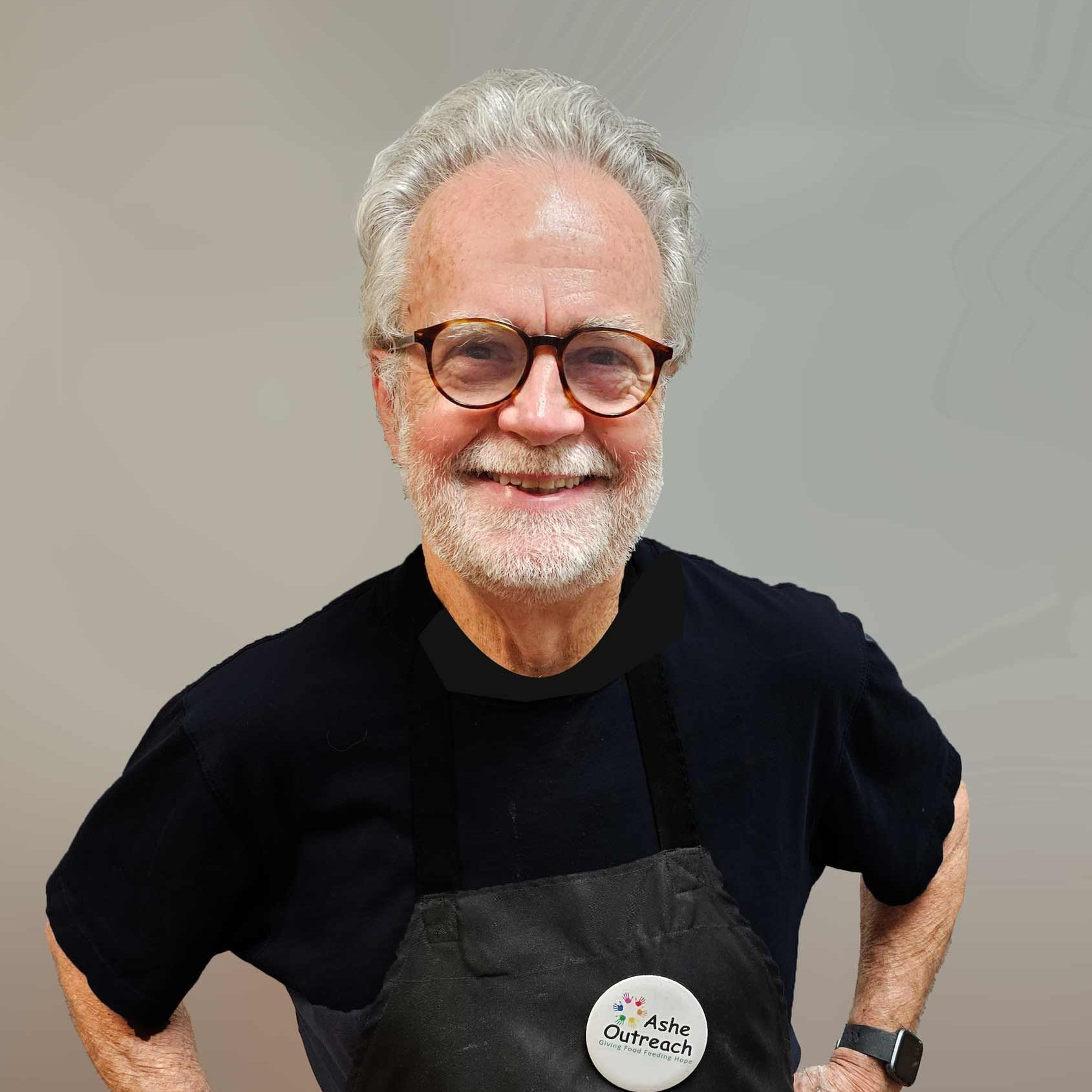 A man wearing glasses and an apron is smiling for the camera.