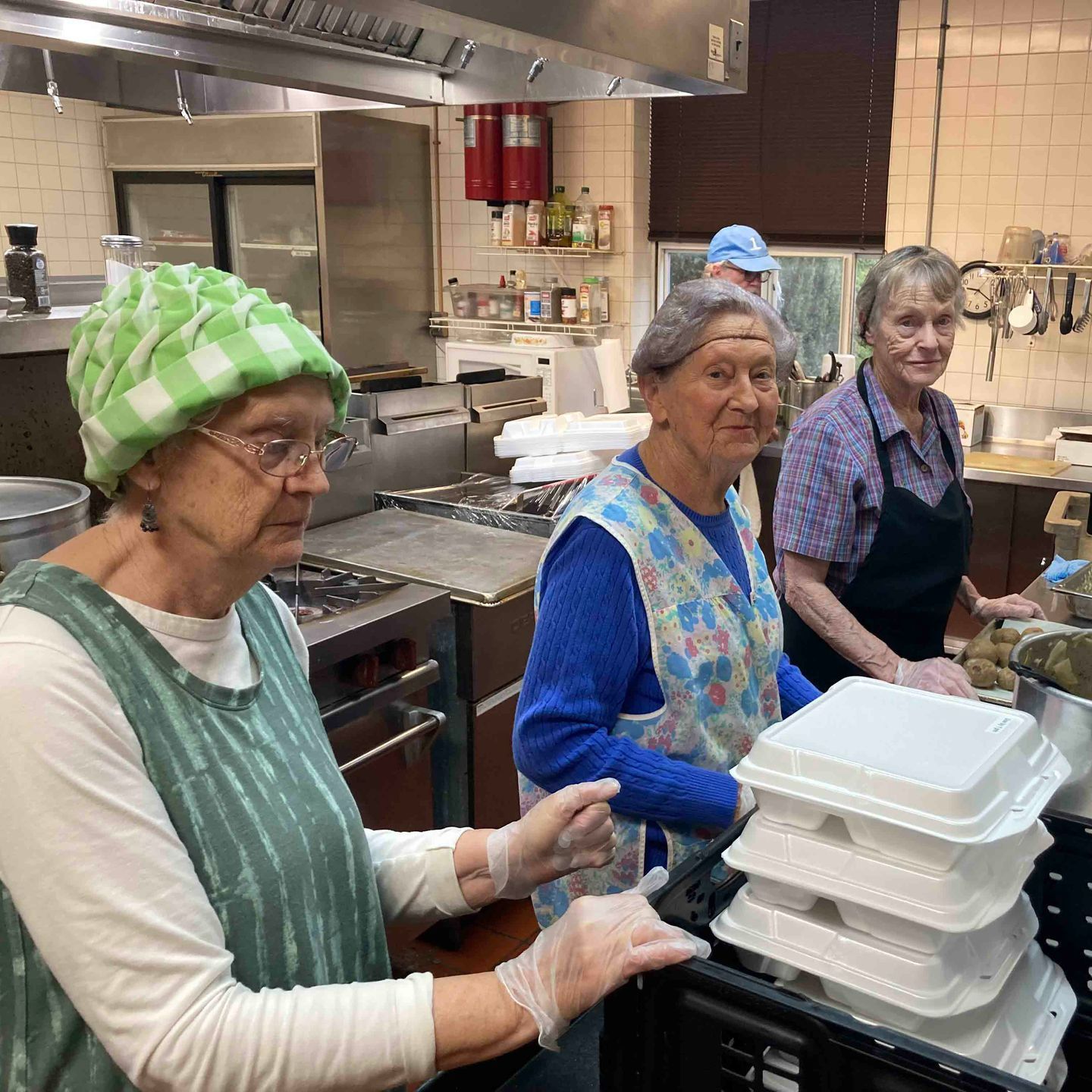 A group of women are standing in a kitchen preparing food.