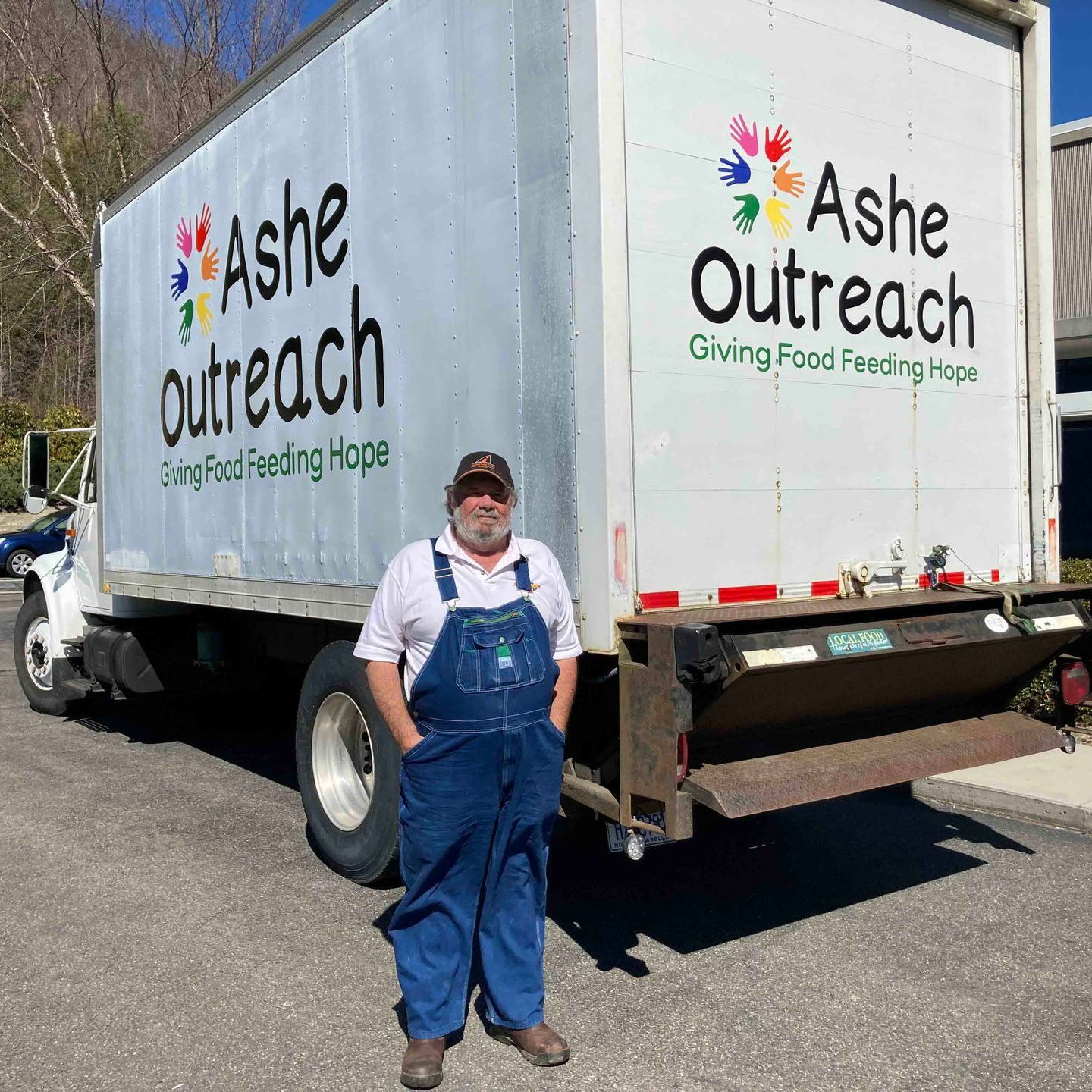 A man in overalls is standing in front of an ash outreach truck