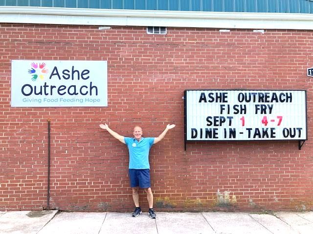 A man is standing in front of a sign that says ashe outreach