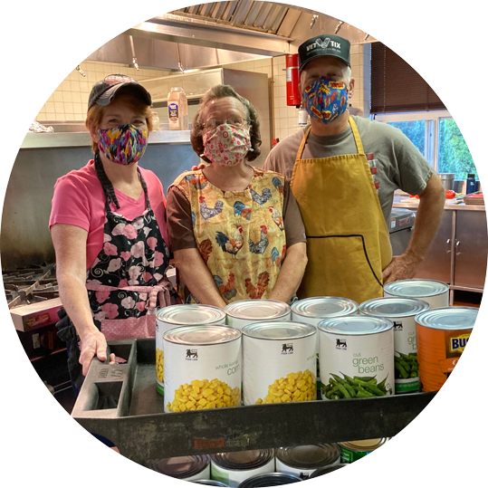 A group of people wearing face masks are standing in a kitchen.