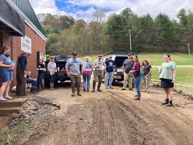A group of people are standing on a dirt road in front of a building.