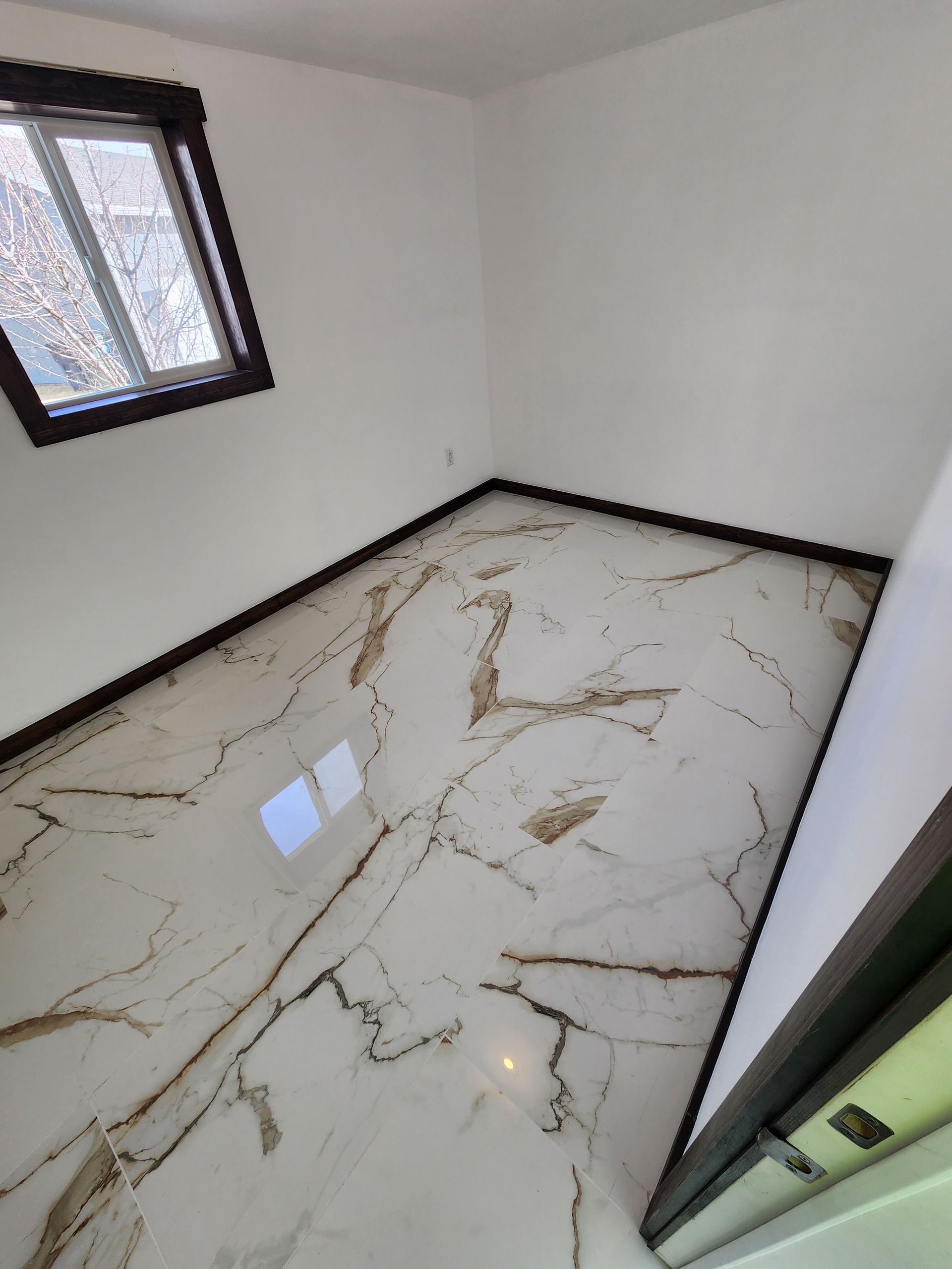 Empty room with white walls, marble-patterned floor, and a dark-framed window.