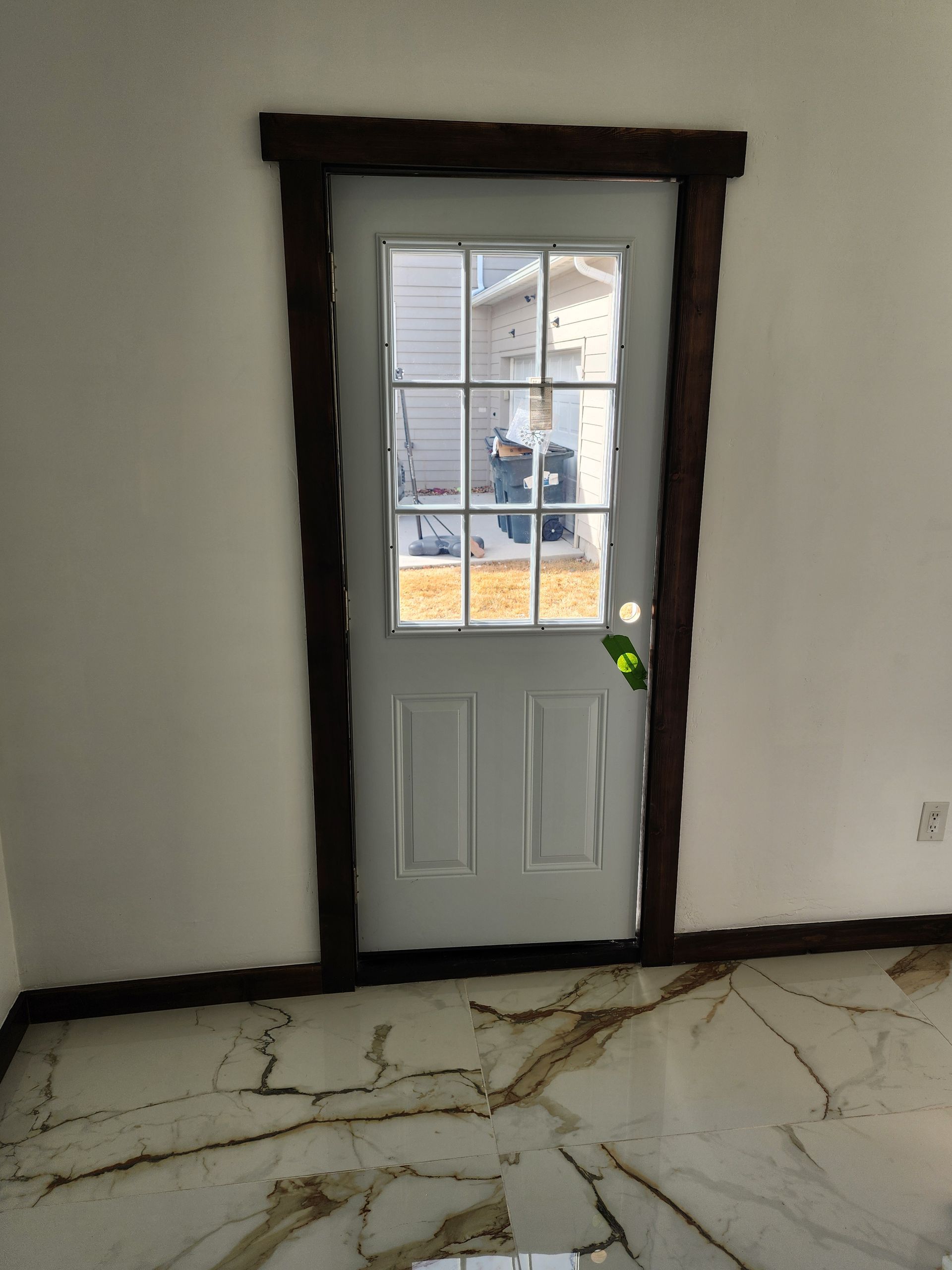 White door with glass panes and dark wood trim in a room with white walls and damaged flooring.