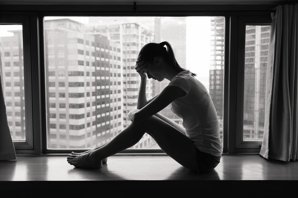 A Sad Woman Is Sitting On A Window — Gold Coast Detox and Rehab Services in Gold Coast, QLD