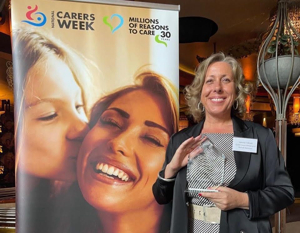 A Woman is Holding a Trophy in Front of a Poster for Carers Week — Gold Coast Detox and Rehab Services in Gold Coast, QLD