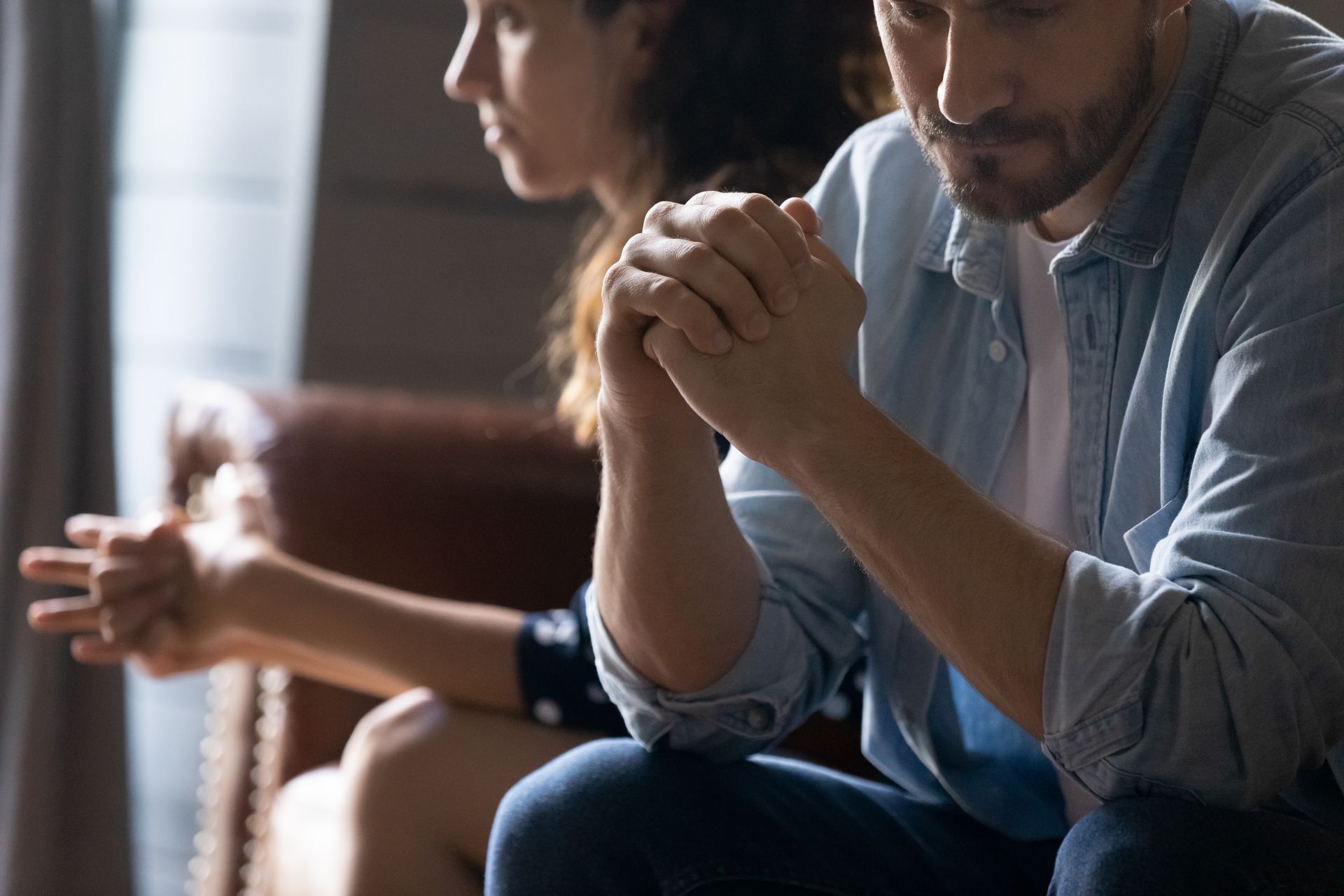 A Man is Beside A Woman Sitting on a Couch Holding His Own Hands — Gold Coast Detox and Rehab Services in Gold Coast, QLD