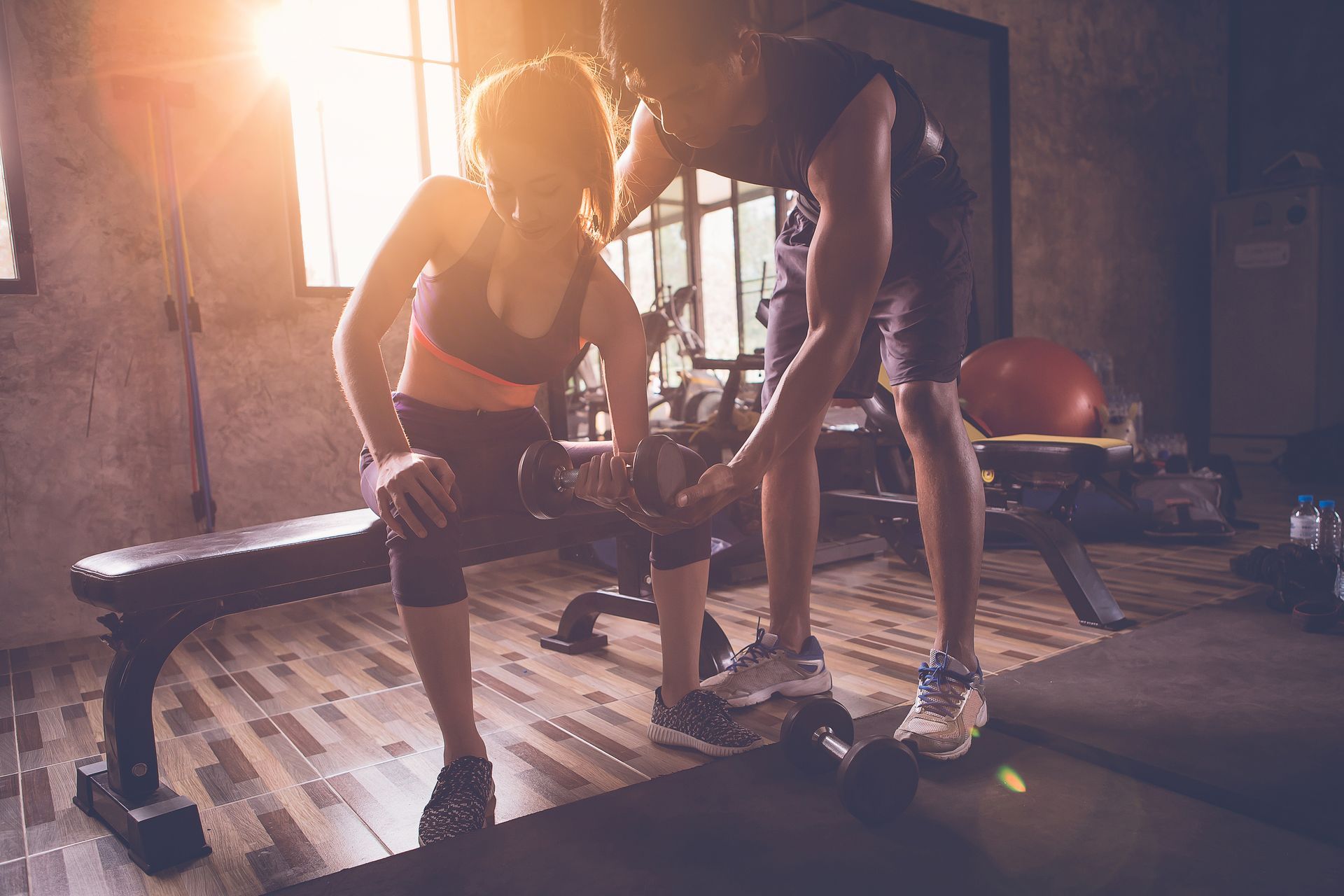 A Man is Helping a Woman Lift a Dumbbell in a Gym — Gold Coast Detox and Rehab Services in Gold Coast, QLD