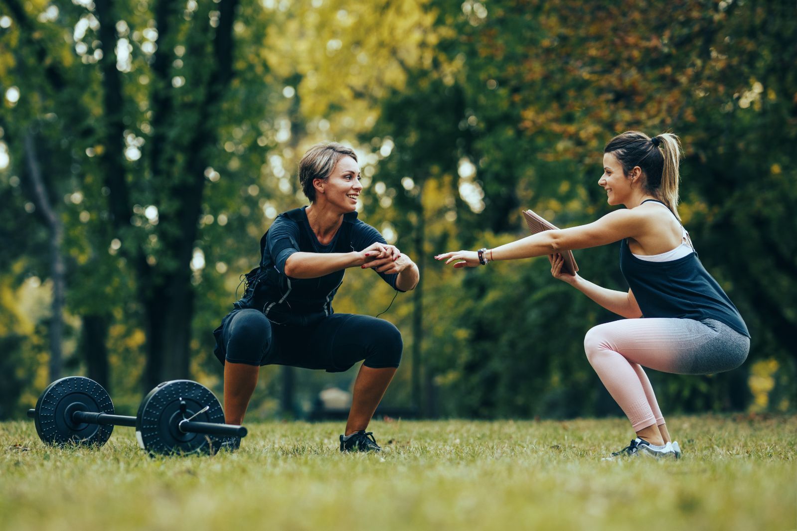 Two Women Are Squatting in a Park With a Barbell — Gold Coast Detox and Rehab Services in Gold Coast, QLD