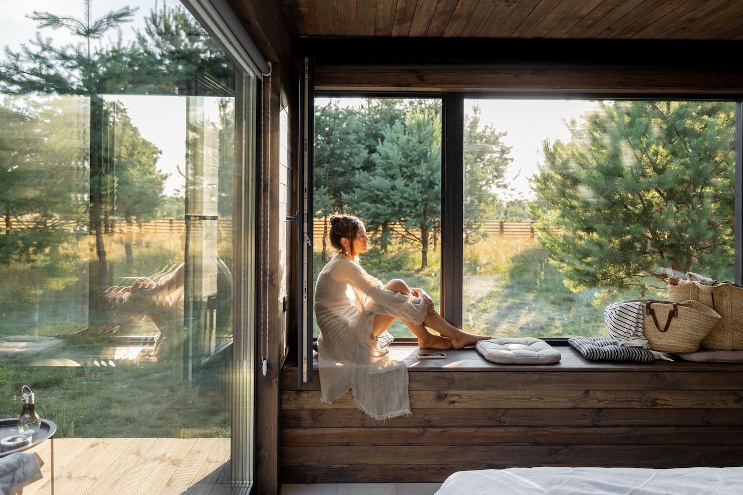 A Woman is Sitting on a Window Sill in a Room Looking Out the Window — Gold Coast Detox and Rehab Services in Gold Coast, QLD