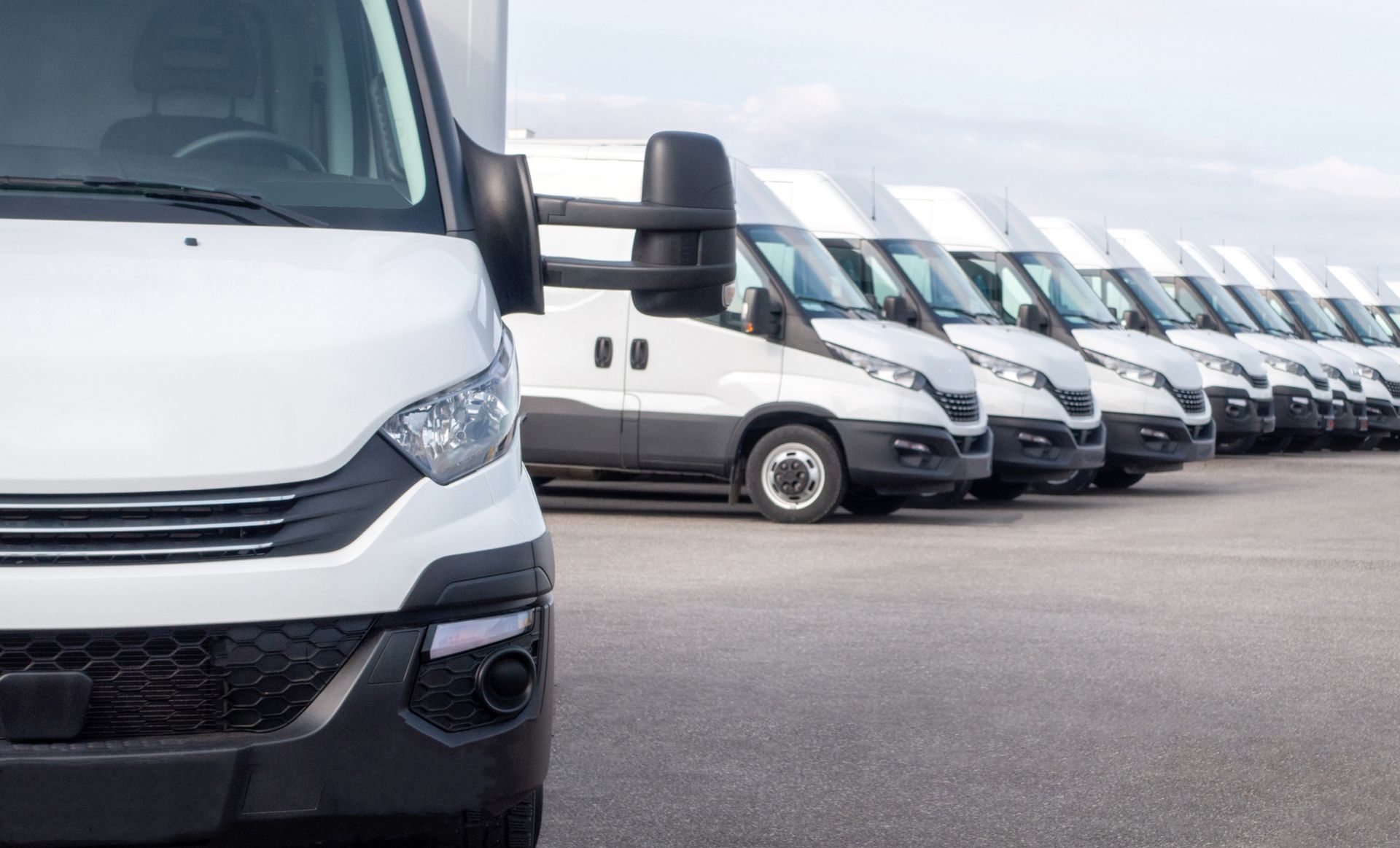 A row of white vans are parked in a parking lot.