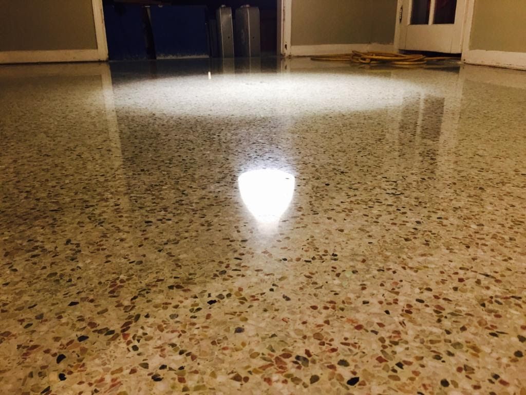 Polished terrazzo flooring with a bright, reflective light source casting a glow on the smooth, speckled surface.