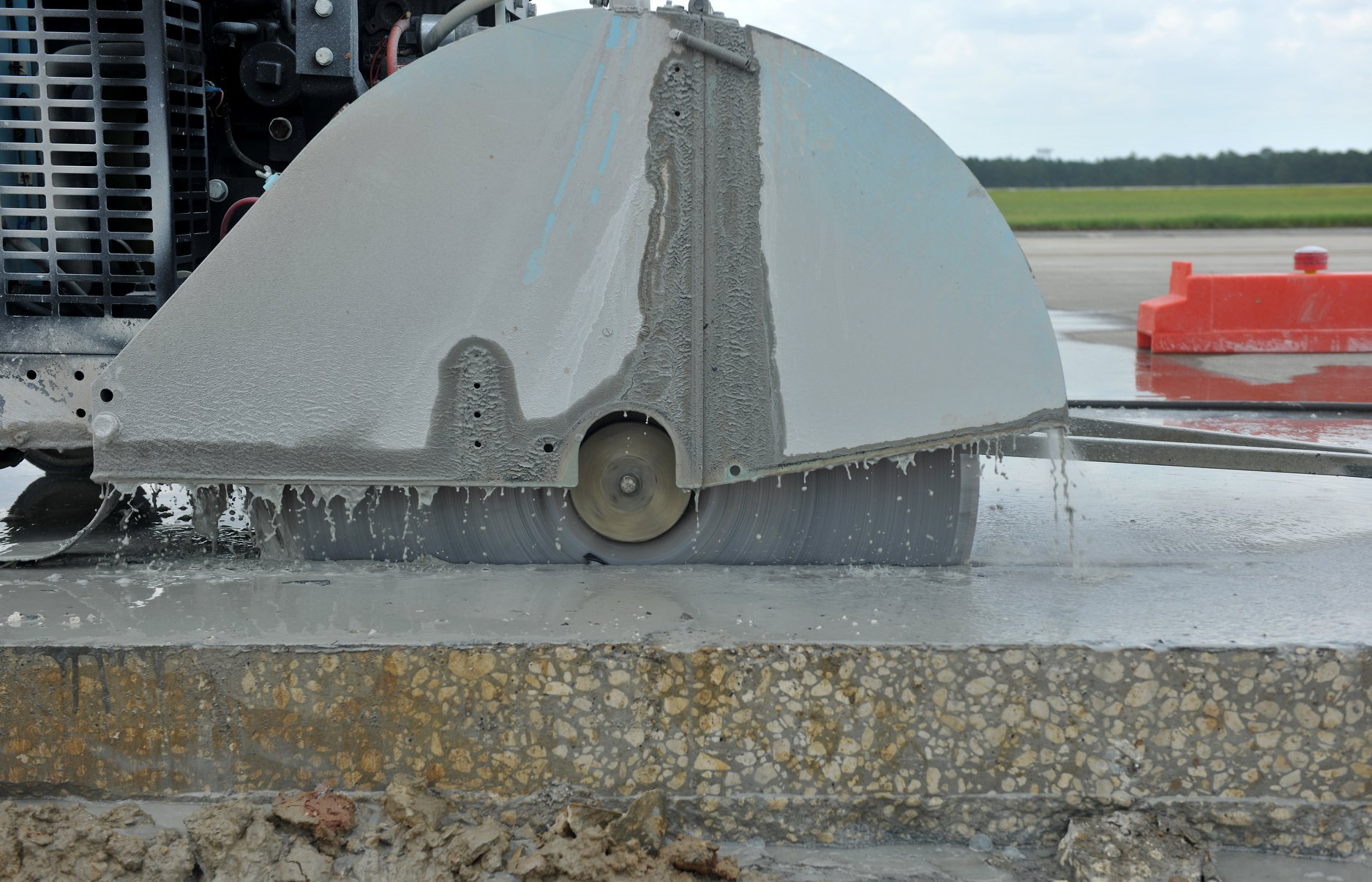A heavy-duty industrial saw cuts through a concrete slab, with water spray visible along the blade.