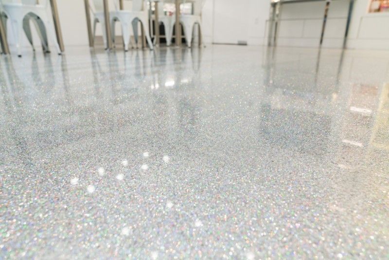 A shiny, light-grey speckled epoxy floor reflecting chairs and indoor lighting in a commercial space.