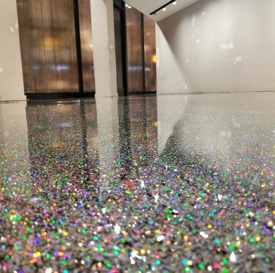 A modern interior with a high-gloss, reflective floor covered in dense, iridescent, multi-colored glitter particles.