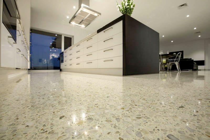 Modern kitchen with a polished, speckled concrete floor and a large white island with a dark accent panel.
