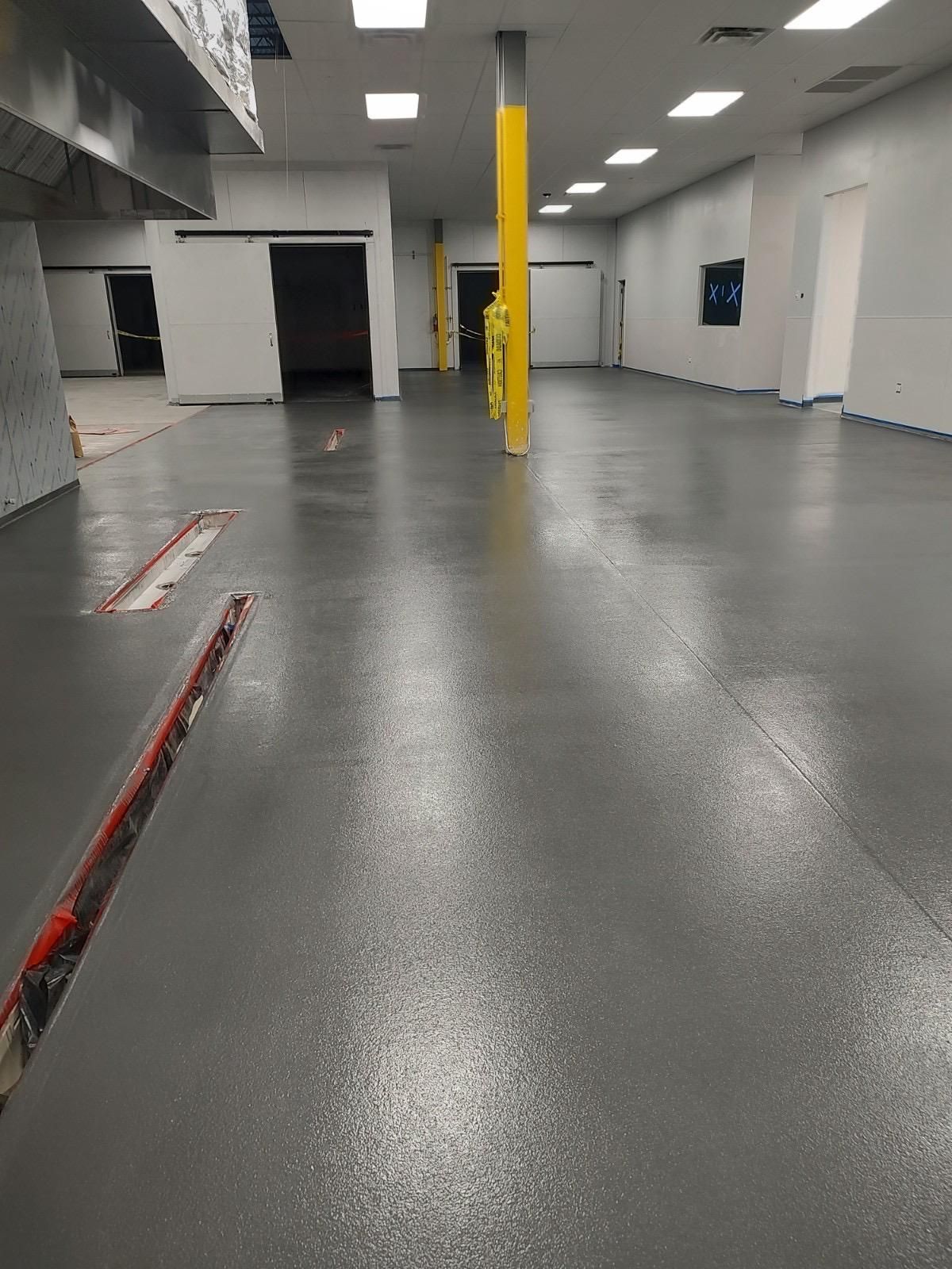 A view of an indoor commercial space with a freshly finished grey epoxy floor, yellow support pillars, and white walls.