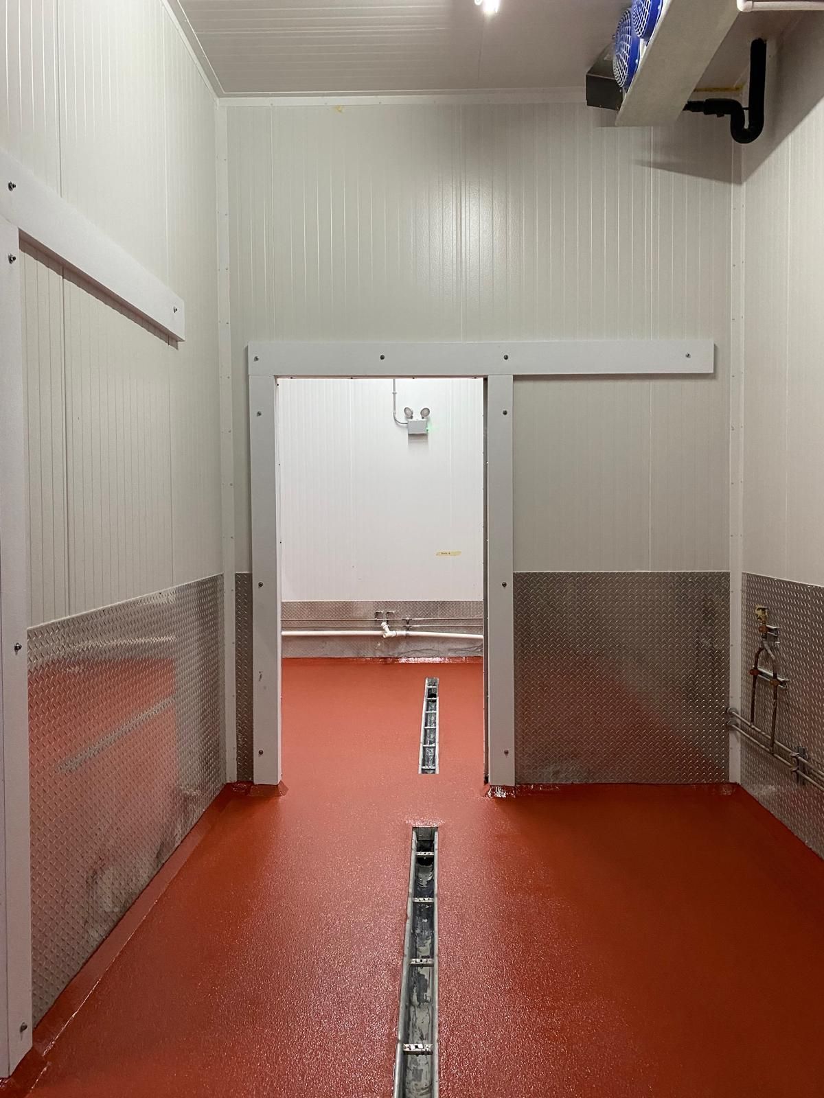 A doorway leads from a terracotta-colored floor into a white room, with diamond-plate metal lining the lower walls.